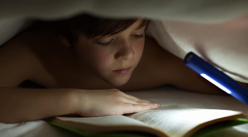 Young boy reading a book under the blanket or quilt - lighting with a flashlight